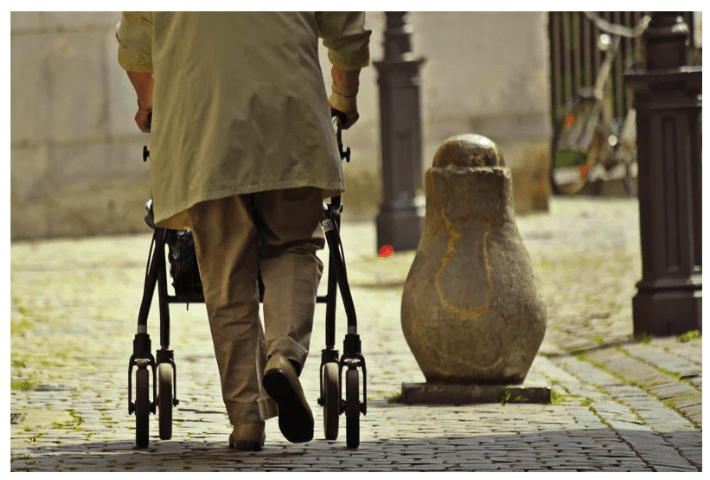 elderly man walking with a walker outside on uneven ground